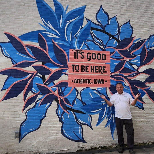 Jared Wockenfuss in front of the It's Good To Be Here mural in Atlantic, Iowa