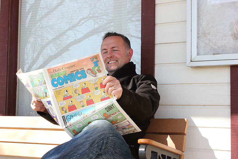 Jared Wockenfuss sitting on a porch bench reading the Sunday comics